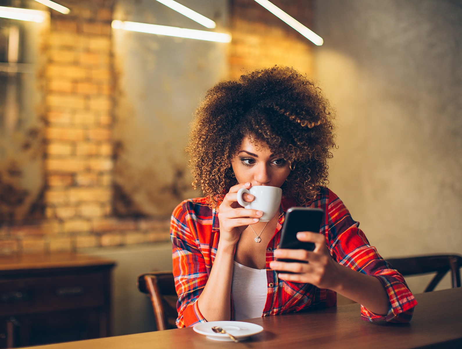woman drinking coffee looking at a cell phone