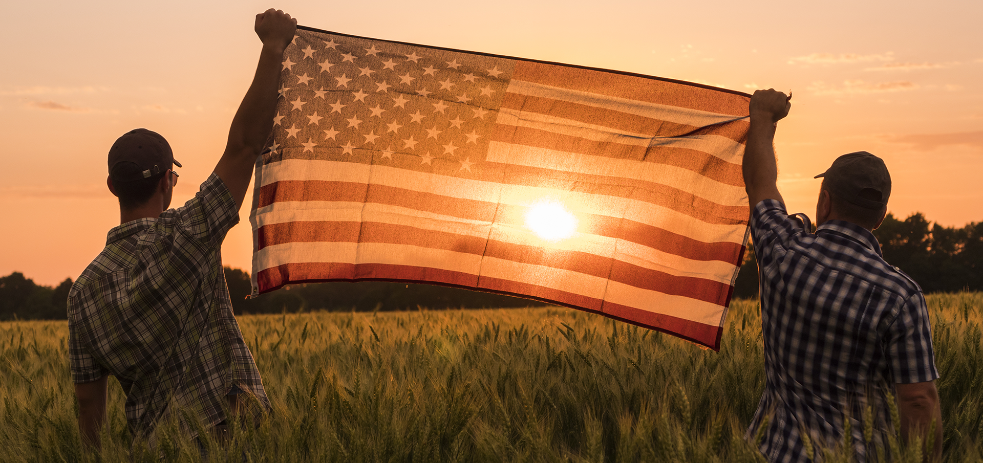 two men holding an American Flag in a field during sunset